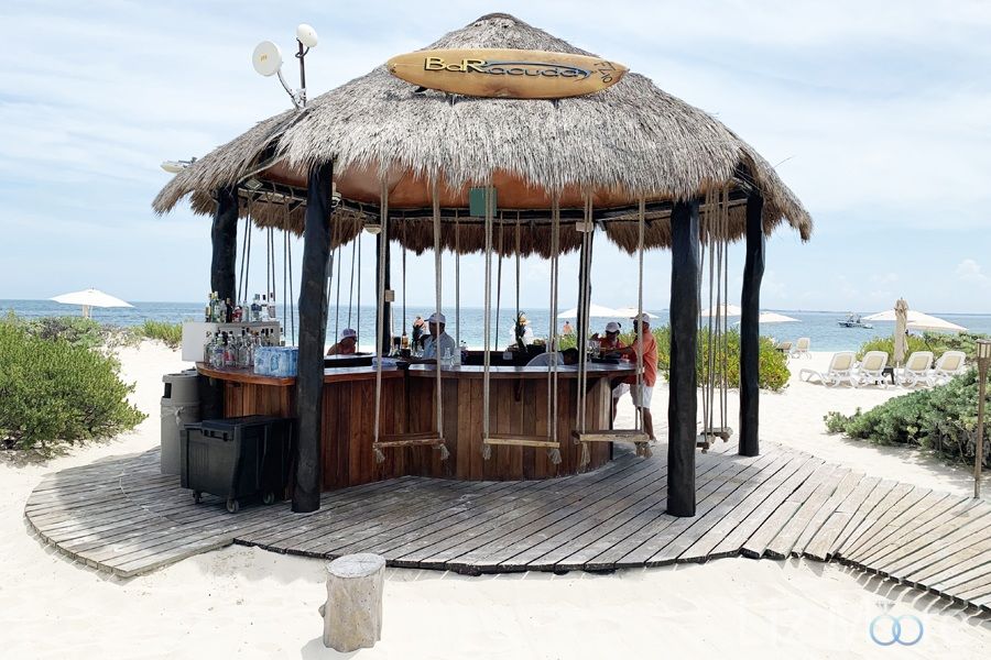 Beach bar set up with swinging chairs and wooden walkway over to the ocean