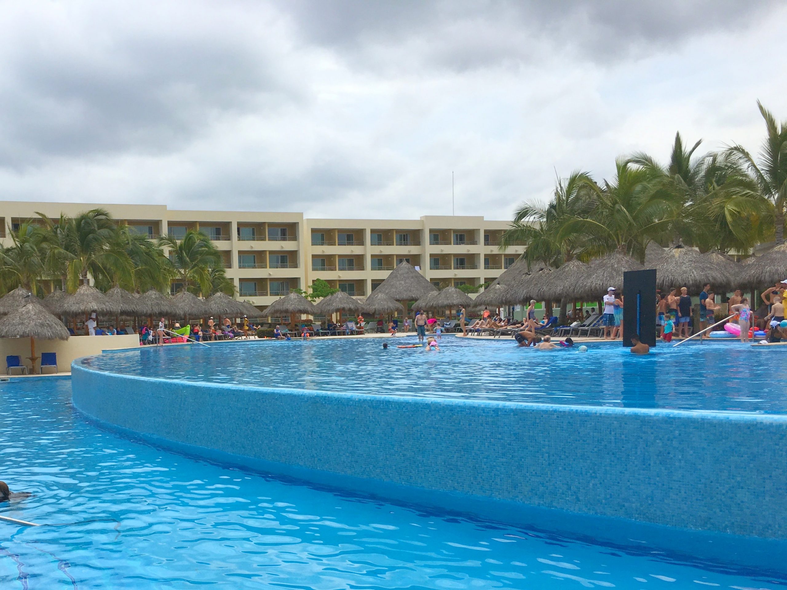 main pool area with infinity pool and beach loungers and guests swimming in the water