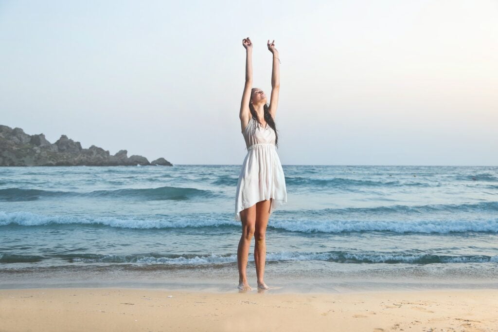 Bride on beach with white dress and hands in the air.